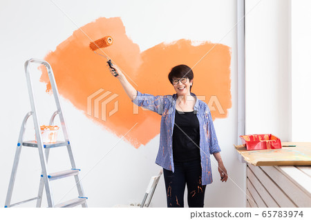 Happy smiling middle-aged woman painting interior wall of new house. Redecoration, renovation, apartment repair and refreshment concept. Happy smiling middle-aged woman painting interior wall of new house. Redecoration, renovation, apartment repair and refreshment concept. 65783974