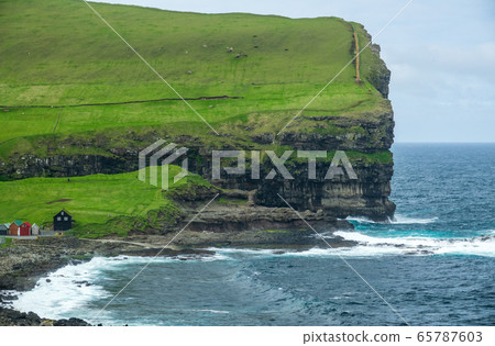 Steep cliffs and hiking tracks in Faroe Islands coastline 65787603
