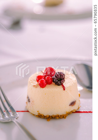 Vanilla and Red Fruits Dessert Cake served with Cookie Base served on a white plate with spoon and fork Vanilla and Red Fruits Dessert Cake served with Cookie Base served on a white plate with spoon and fork 65790835