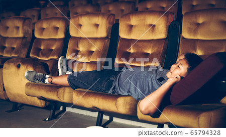 A boy laying down on armchair in cinema. A boy laying down on armchair in cinema. 65794328