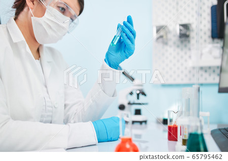 Close up of laboratory technician in blue rubber gloves holding test tube. Close up of laboratory technician in blue rubber gloves holding test tube. 65795462