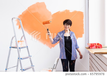 Beautiful middle-aged female painting the wall with paint roller. Portrait of a young beautiful woman painting wall in her new apartment. Redecoration and renovation concept. Beautiful middle-aged female painting the wall with paint roller. Portrait of a young beautiful woman painting wall in her new apartment. Redecoration and renovation concept. 65795978