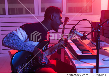 African american professional musician recording bass guitar in digital studio at home, music production technology concept. African american professional musician recording bass guitar in digital studio at home, music production technology concept. 65796041