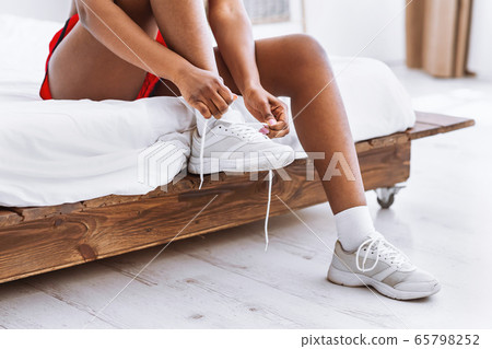 African american girl sitting on bed and putting on shoes 65798252
