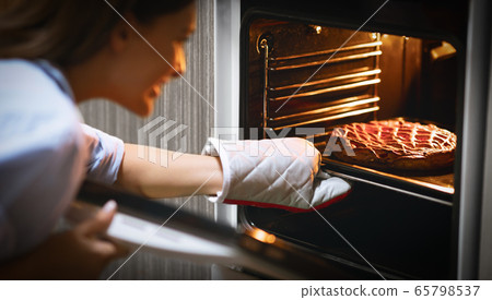 Young housewife removing fresh pie out of oven at home Young housewife removing fresh pie out of oven at home 65798537
