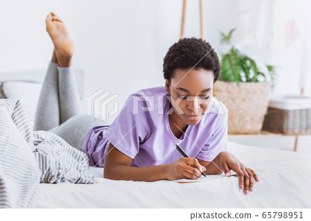 Thoughts written in diary. Girl lies in bed and makes notes in notebook 65798951