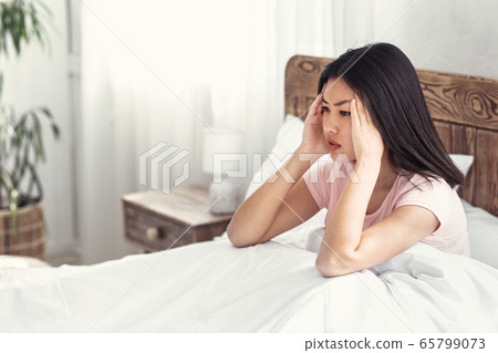Asian Girl Having Migraine Pain Sitting In Bed At Home 65799073