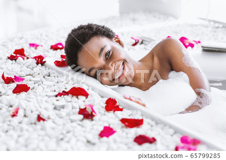 Spa day and beauty care at home. Woman takes bath with foam and petals Spa day and beauty care at home. Woman takes bath with foam and petals 65799285