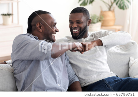 Father-Son Friendship. Black Millennial Guy Bumping Fists With Senior Dad At Home 65799751