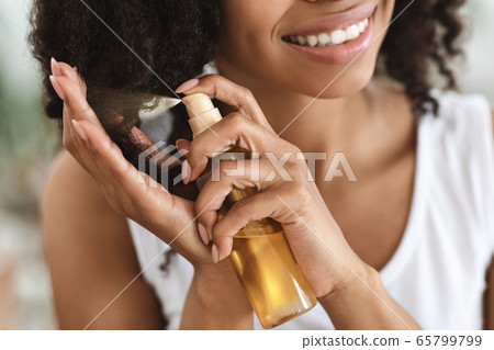 Split Ends Treatment. Smiling Black Woman Spraying Essential Oil On Curly Hair 65799799