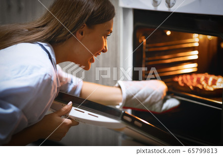 Cheerful woman taking fresh pie from oven at kitchen Cheerful woman taking fresh pie from oven at kitchen 65799813