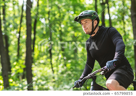 Man in helmet cyclist riding bike in forest 65799855
