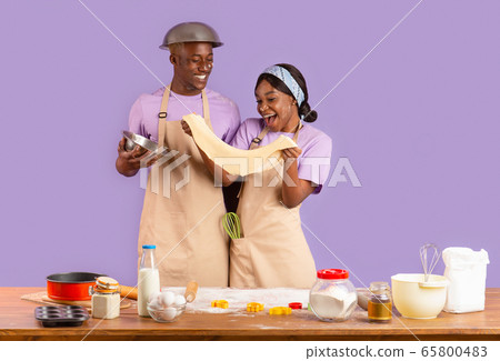 Romantic cooking times. Young black couple with dough baking on lilac background Romantic cooking times. Young black couple with dough baking on lilac background 65800483