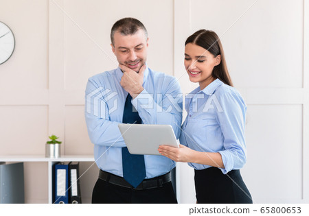 Businesswoman Showing Tablet Computer To Colleague Businessman Standing In Office 65800653