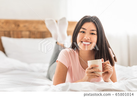 Asian Girl Having Coffee Lying In Bed In Cozy Bedroom Asian Girl Having Coffee Lying In Bed In Cozy Bedroom 65801014