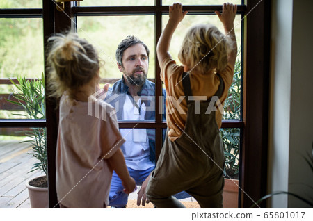 Doctor coming to see family in isolation, window glass separating them. Doctor coming to see family in isolation, window glass separating them. 65801017
