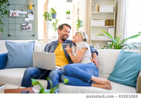 Happy couple in love sitting indoors at home, using laptop. 65801088
