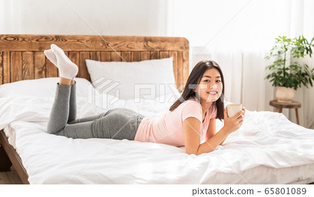 Asian Woman Enjoying Morning Coffee Lying In Bed At Home 65801089