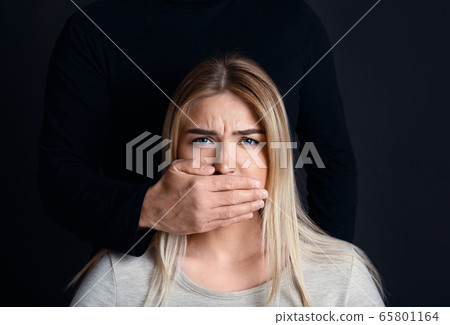 Man hand is cover mouth of despaired scared girl, with black silhouette behind 65801164