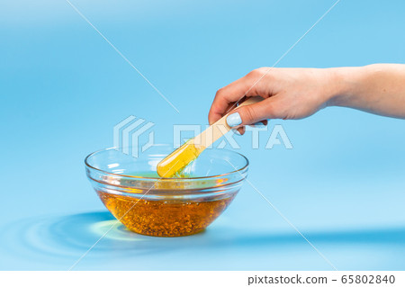 Depilation and beauty concept - sugar paste or honey wax for hair removing spatula with wooden framing sticks on a bright blue background Depilation and beauty concept - sugar paste or honey wax for hair removing spatula with wooden framing sticks on a bright blue background 65802840