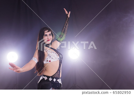 Young woman belly dancer in exotic dress with gold, dancing tribal fusion dance in studio. Copy space. 65802950