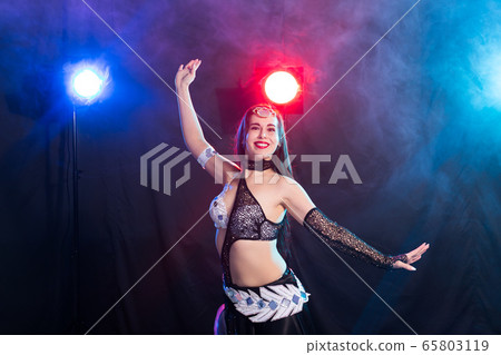 Young woman belly dancer in exotic dress with gold, dancing tribal fusion dance in studio. Young woman belly dancer in exotic dress with gold, dancing tribal fusion dance in studio. 65803119