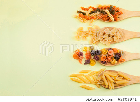 various pasta of Italian cuisine. Farfalle, penne rigate, fusilli on wooden spoons on a yellow background. Top view, copy space. various pasta of Italian cuisine. Farfalle, penne rigate, fusilli on wooden spoons on a yellow background. Top view, copy space. 65803971