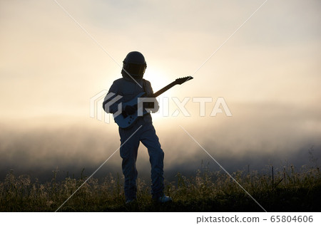Astronaut standing on grass and playing guitar. 65804606