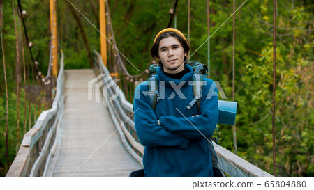 Young man traveler standing on the bridge and looking in the camera Young man traveler standing on the bridge and looking in the camera 65804880