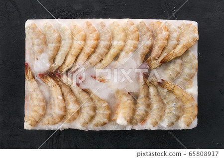 Raw tiger shrimp frozen in large ice cube on black background 65808917