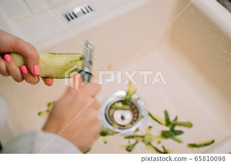 Woman cleans cucumber in the sink in kitchen  65810098