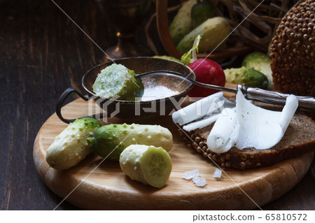 Wooden tray with mini cucumbers, salt shaker and black bread sandwich with lard Wooden tray with mini cucumbers, salt shaker and black bread sandwich with lard 65810572
