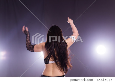 Young woman belly dancer in exotic dress with gold, dancing tribal fusion dance in studio. Back view. Young woman belly dancer in exotic dress with gold, dancing tribal fusion dance in studio. Back view. 65813047