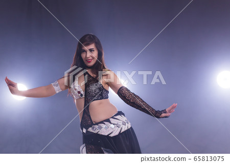 Young woman belly dancer in exotic dress with gold, dancing tribal fusion dance in studio. Young woman belly dancer in exotic dress with gold, dancing tribal fusion dance in studio. 65813075