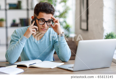 Stressed ethnic freelancer speaking on smartphone. 65813145