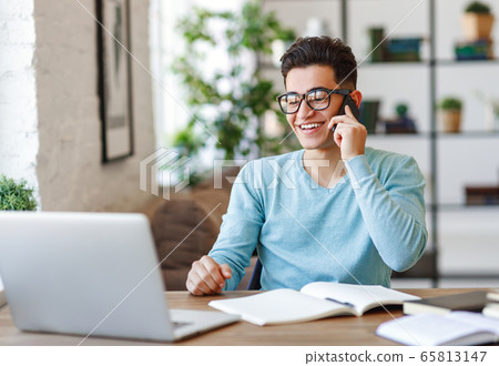 Cheerful ethnic freelancer answering phone call 65813147