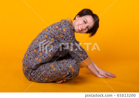 Excited young woman with black hair in home wear pajama, widely smiling having fun. Isolated on yellow background. Copy spase. 65813200