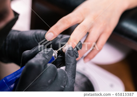Manicurist use electric nail file drill in beauty salon. Perfect nails manicure process close up with burst flying debris. Manicurist use electric nail file drill in beauty salon. Perfect nails manicure process close up with burst flying debris. 65813387