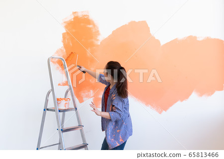 Dancing funny woman painting interior wall of home with paint roller. Redecoration, renovation, apartment repair and refreshment concept. 65813466