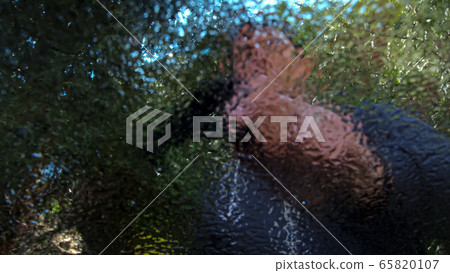High quality close-up of a blurred man wiping wet window glass and holding spray bottle on a bright summer nature background. 65820107