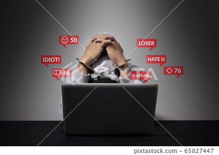cyber bullying concept. A handcuffed man is accused of being a social defendant, bending his head in front of the laptop computer with hate speech as a cyber bullying popup message from social media. cyber bullying concept. A handcuffed man is accused of being a social defendant, bending his head in front of the laptop computer with hate speech as a cyber bullying popup message from social media. 65827447