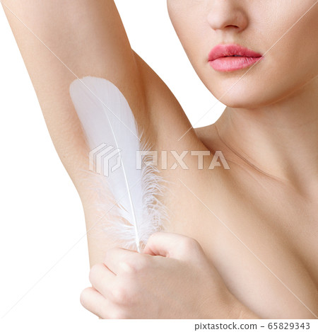 Woman holds white feather near clean armpit. Depilation concept. 65829343