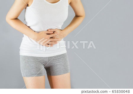 young woman in white undershirt and gray shorts , grabbing belly, She have a stomachache . Health Care Concept. 65830048