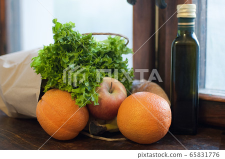 Product set on the wooden windowsill. Green salad, fruits and bottle with oil lying near blue protective gloves. Delivery food during a Coronavirus pandemic and isolation. Product set on the wooden windowsill. Green salad, fruits and bottle with oil lying near blue protective gloves. Delivery food during a Coronavirus pandemic and isolation. 65831776
