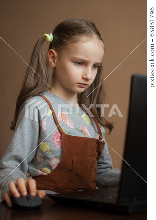 Serious little girl is concentrated in front of her black laptop while focused on doing homework during the quarantine because of the pandemia of Coronavirus Covid-19. Remote education 65831796
