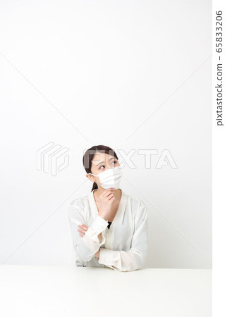 A woman wearing a mask and arms folded while sitting 65833206