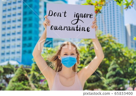 woman in medical mask prevents coronavirus disease holds a poster DON'T IGNORE QUARANTINE Hand woman in medical mask prevents coronavirus disease holds a poster DON'T IGNORE QUARANTINE Hand 65833400