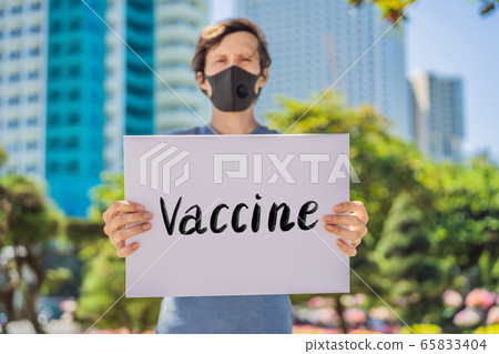 Man in medical mask prevents coronavirus disease holds a poster vaccine Hand written text - Man in medical mask prevents coronavirus disease holds a poster vaccine Hand written text - 65833404