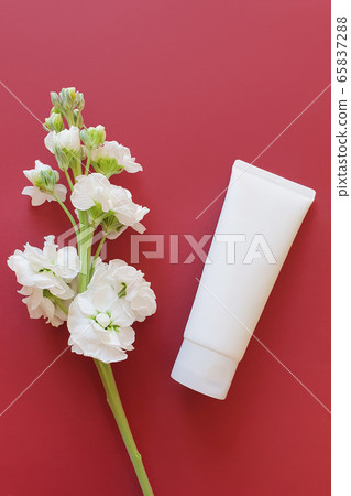 blank white squeeze bottle plastic tube on a burgundy background with a white flower.  View from above, space for a text.  65837288