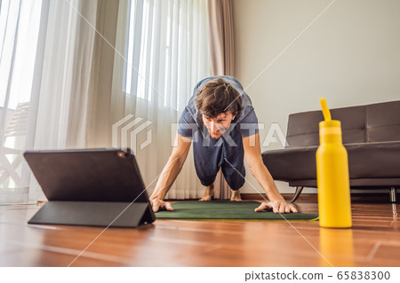 Fitness man exercising on the floor at home and watching fitness videos in a tablet. People do 65838300